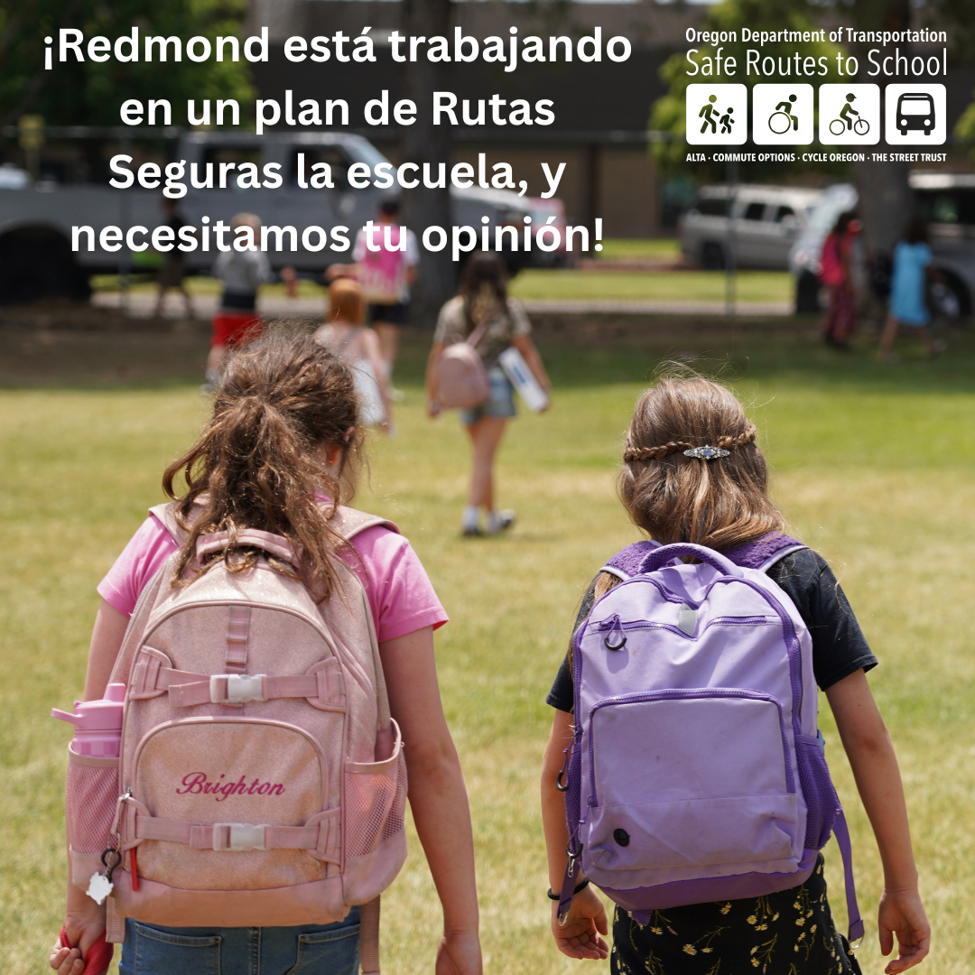 Two children with backpacks walk across a grassy field, viewed from behind.