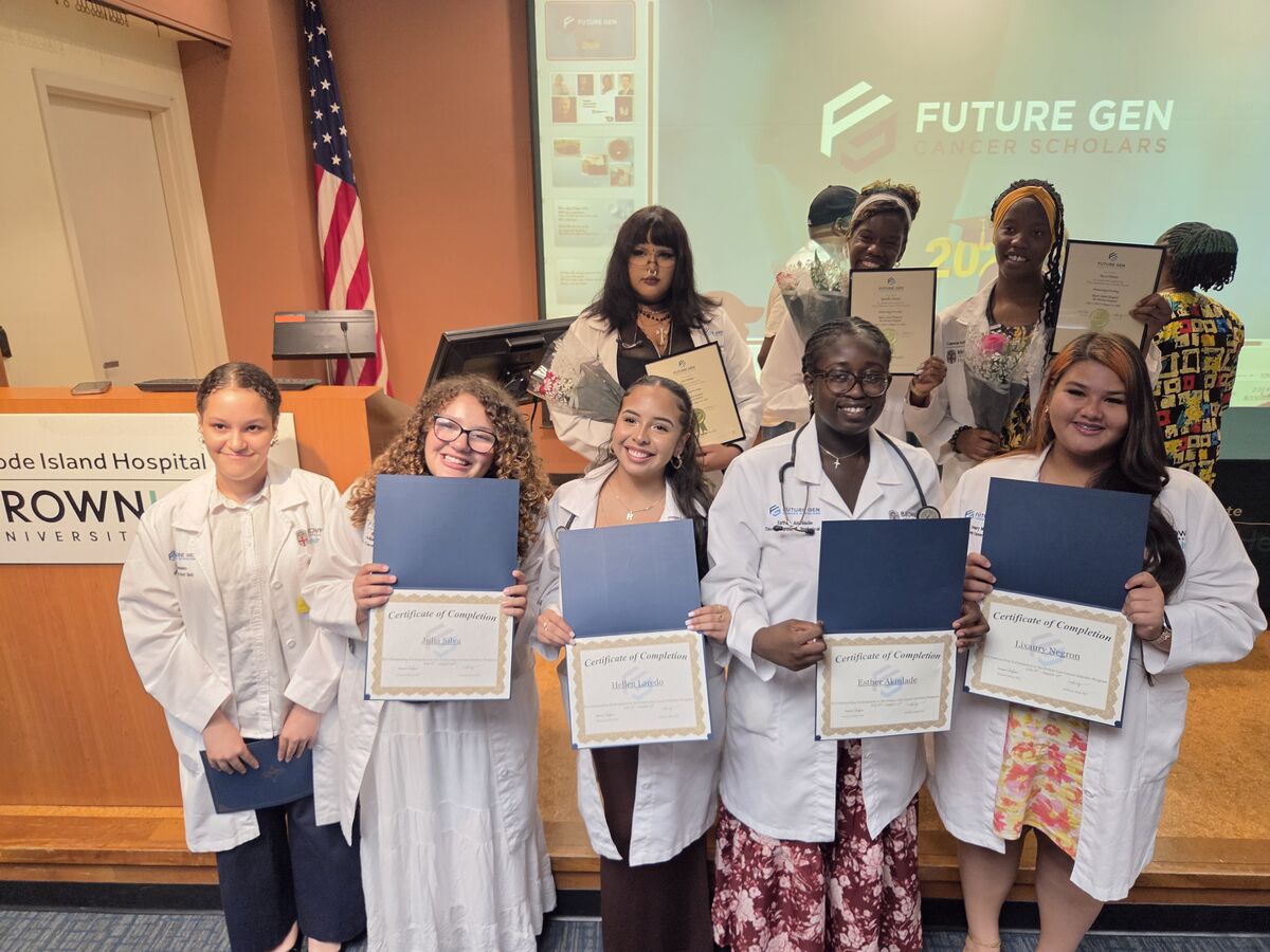 A group of young women in lab coats proudly hold certificates from the "Future Gen Cancer Scholars" program.