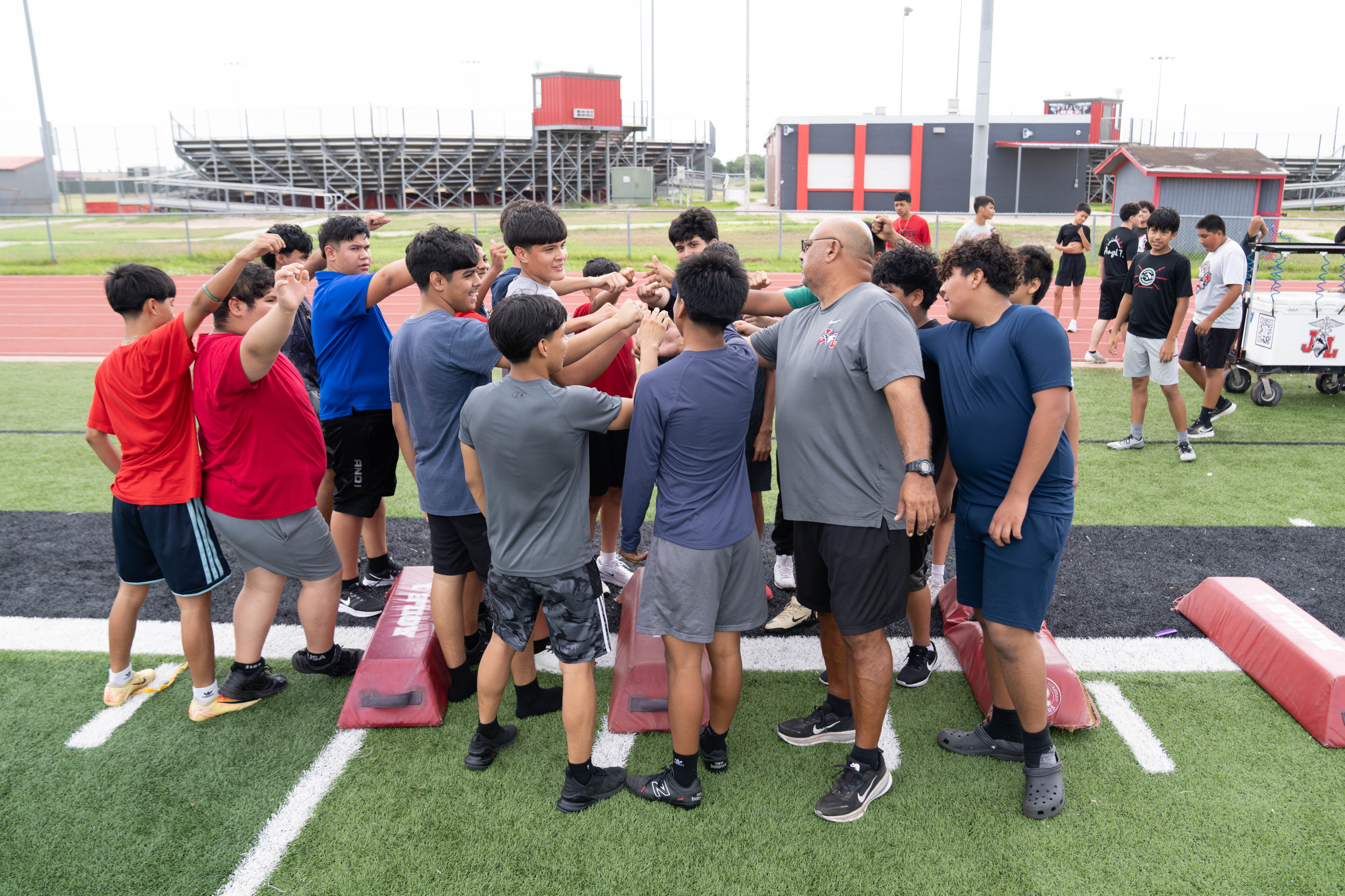 A group of young athletes and a coach huddle together, bumping fists on a sports field.