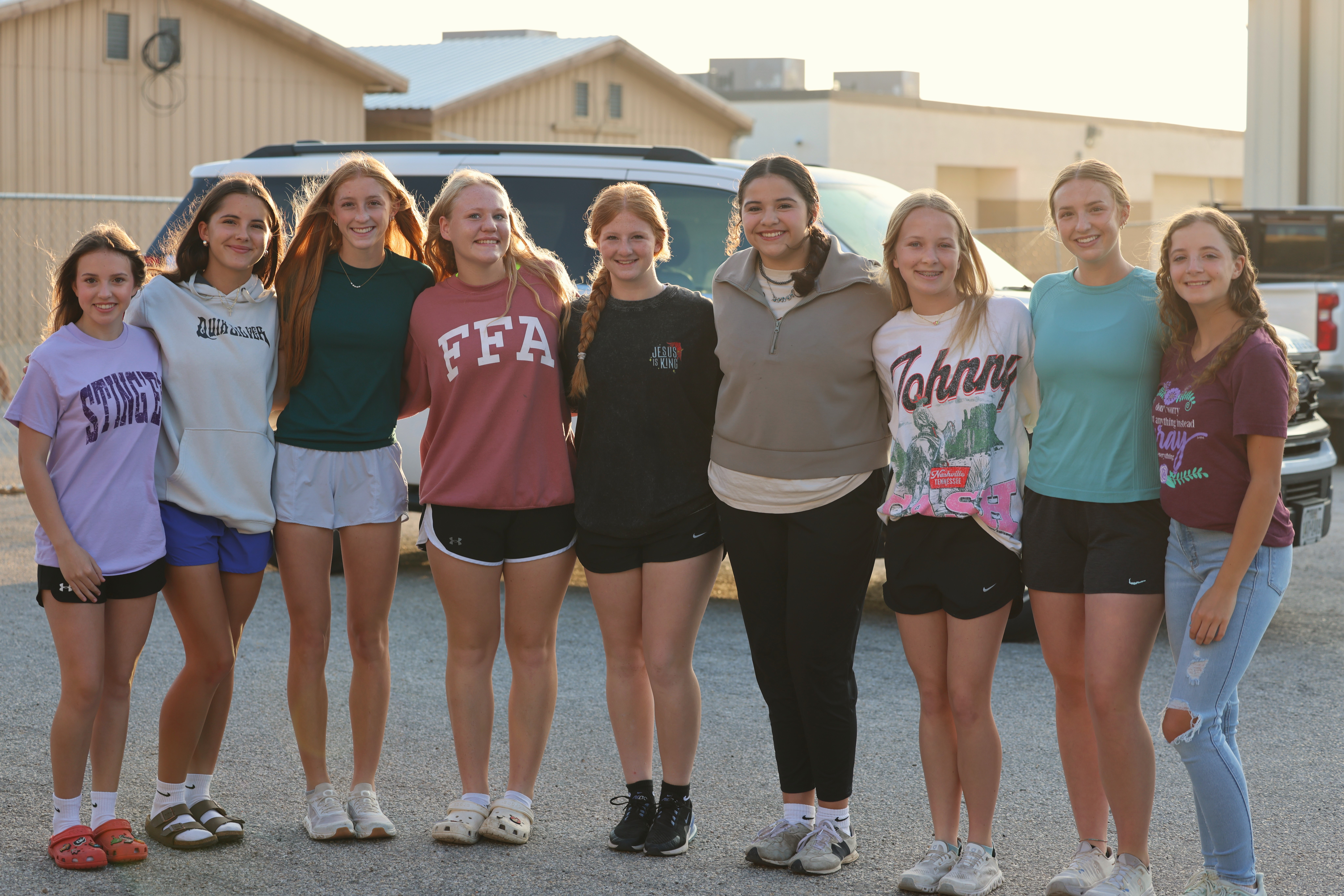 A group of eight young women stand together outdoors, smiling at the camera.