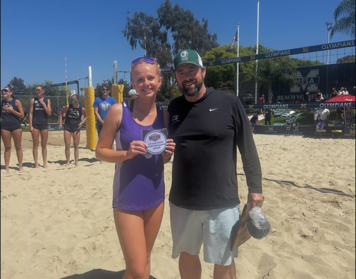 A woman in a purple tank top holds a sportsmanship award on a sandy beach volleyball court.