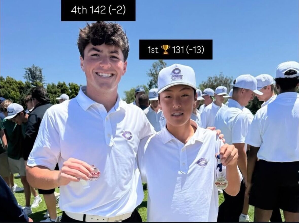 Two young golfers, one holding a medal, pose for a photo with a group of peers in the background.