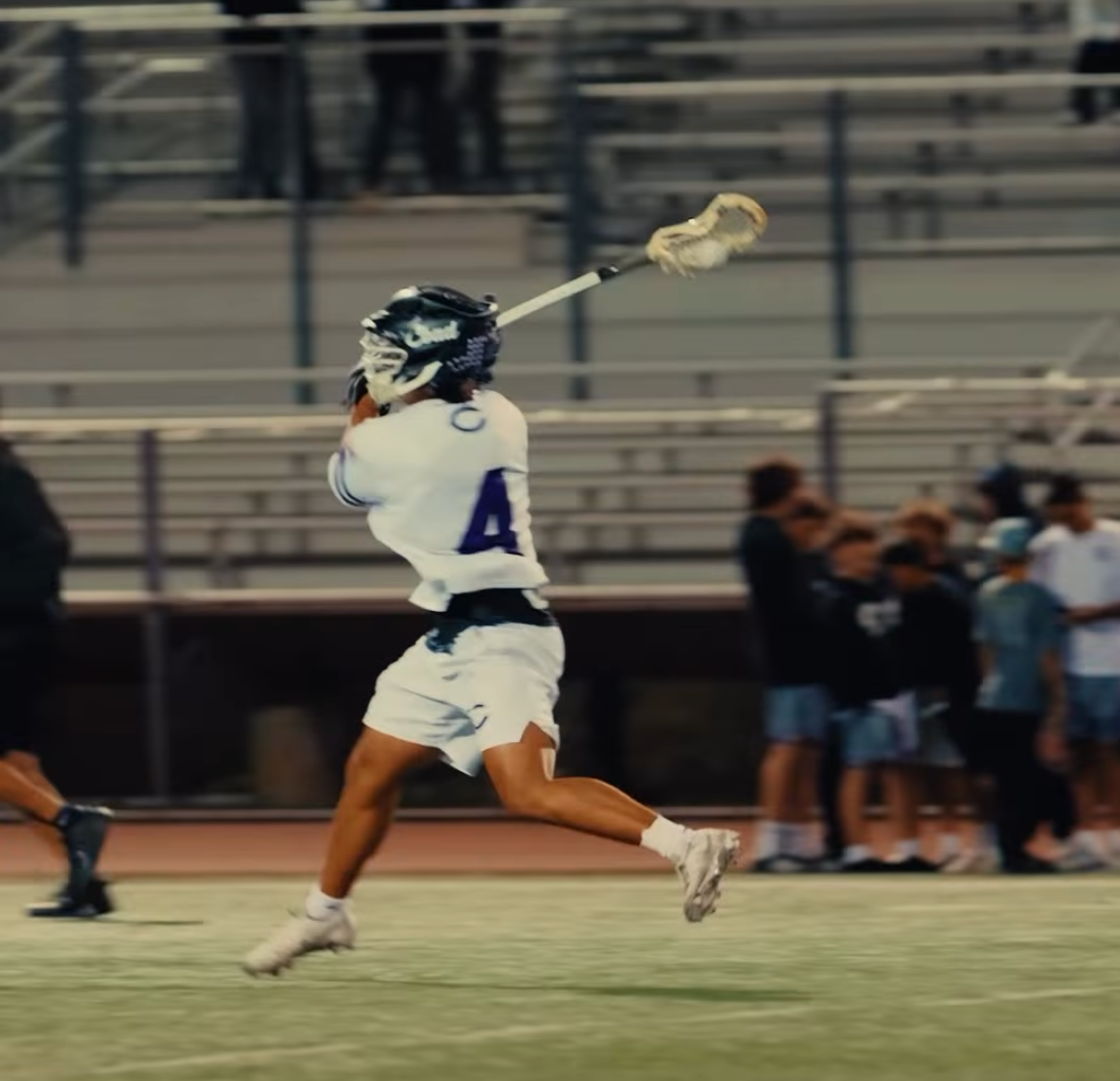 A lacrosse player in a white uniform with the number 4 on the back swings their stick.