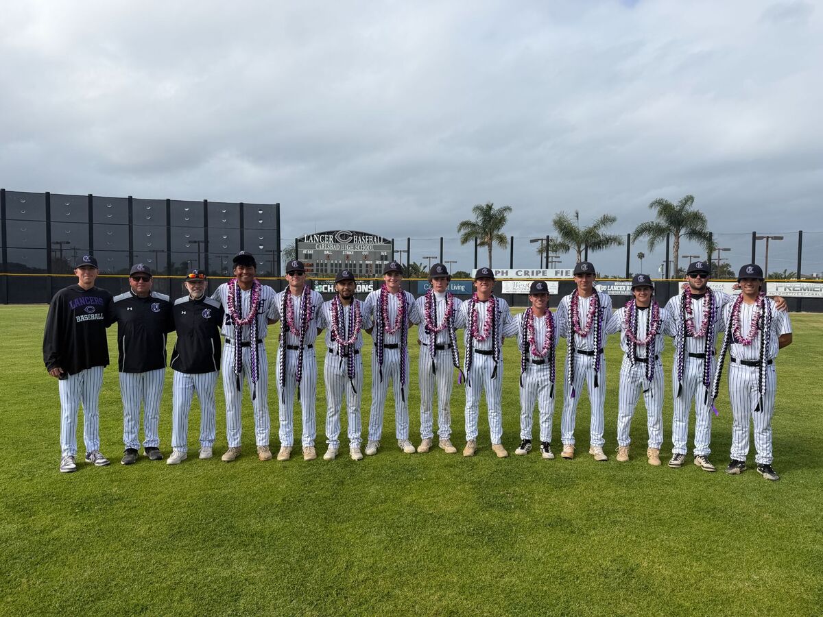 A baseball team and coaches stand on a grassy field, wearing pinstripe uniforms and leis.