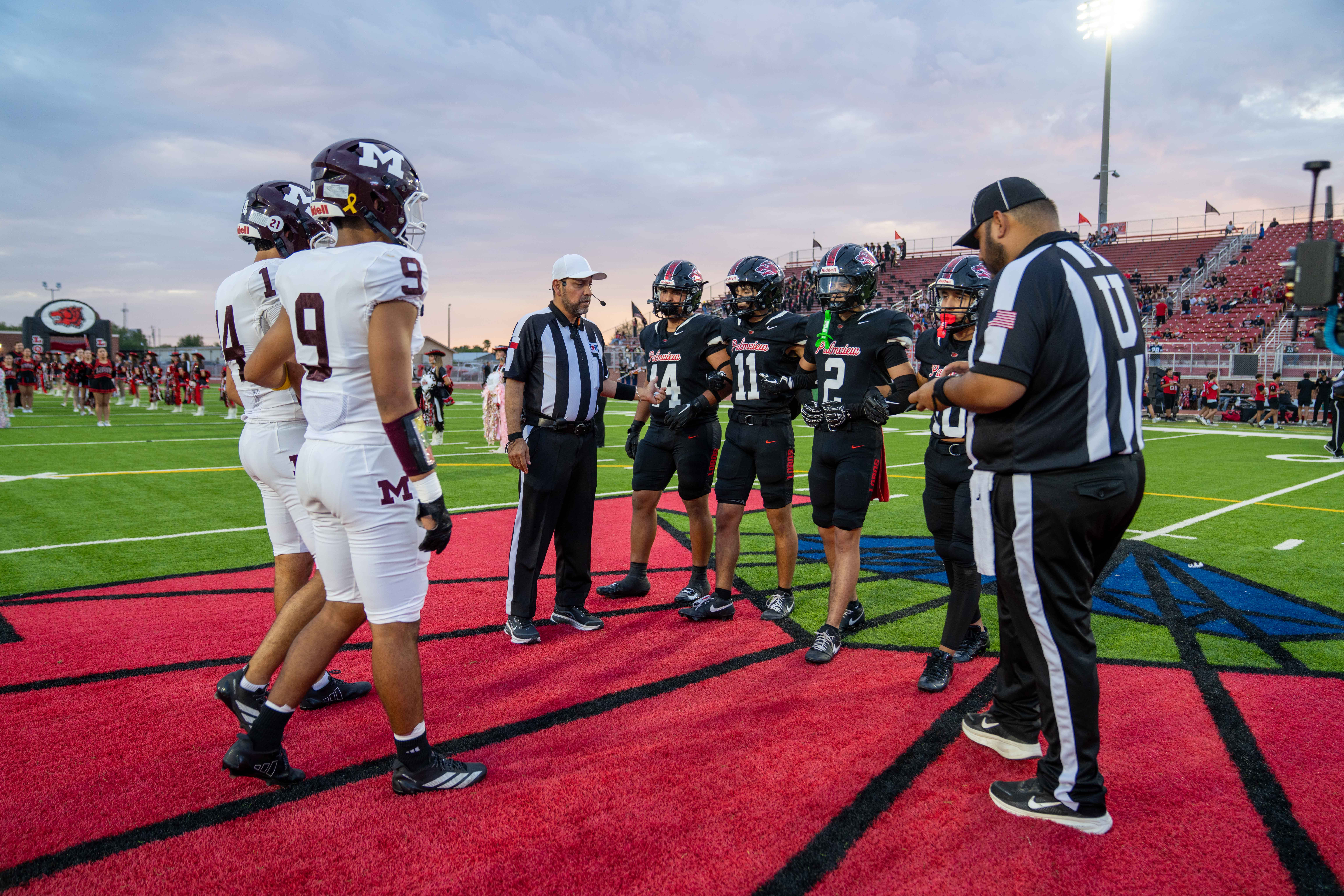 Football players from two teams stand on the field talking with referees before the game.