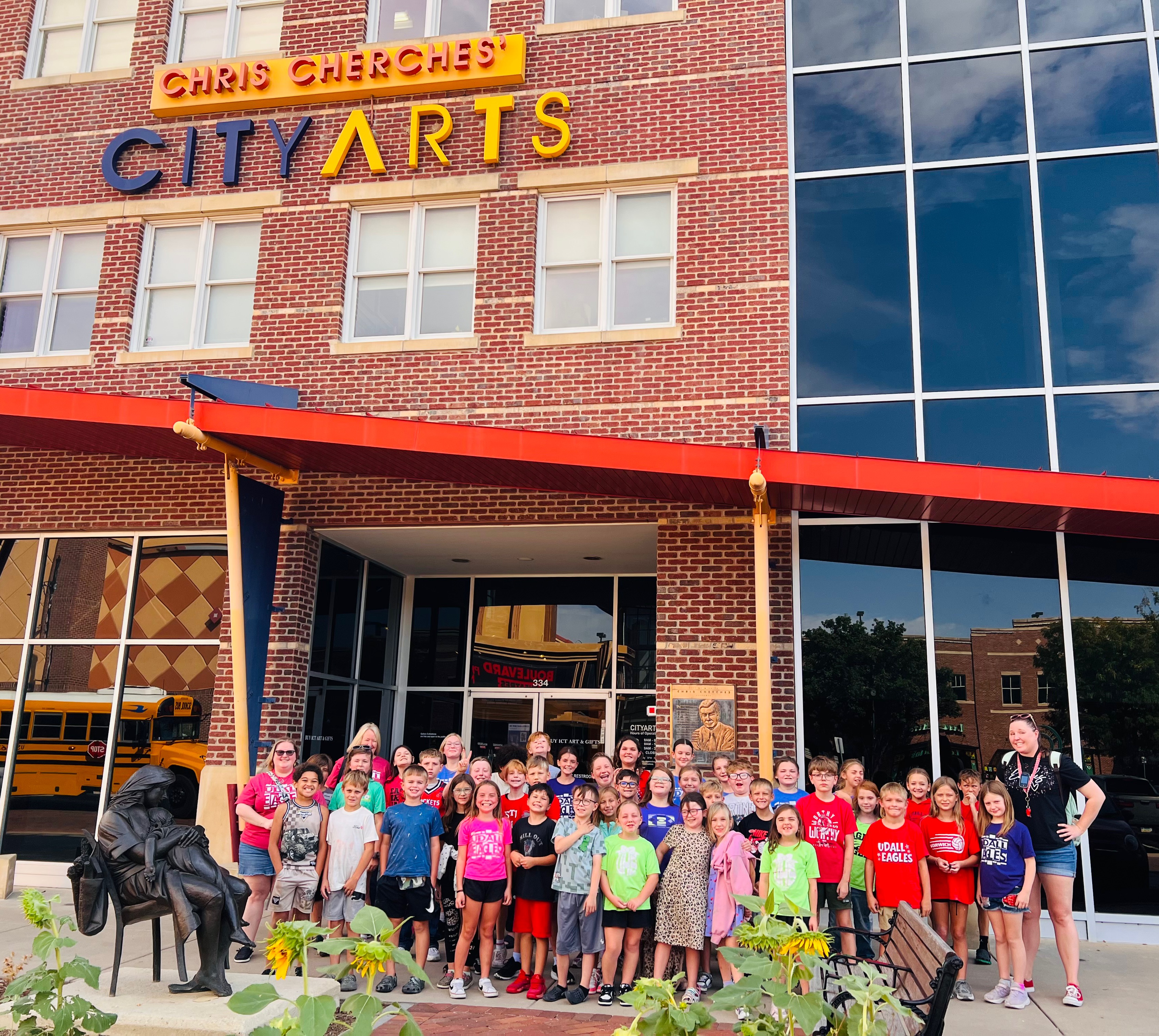 A large group of children and adults pose for a photo outside the red brick building of Chris Cherches CityArts.