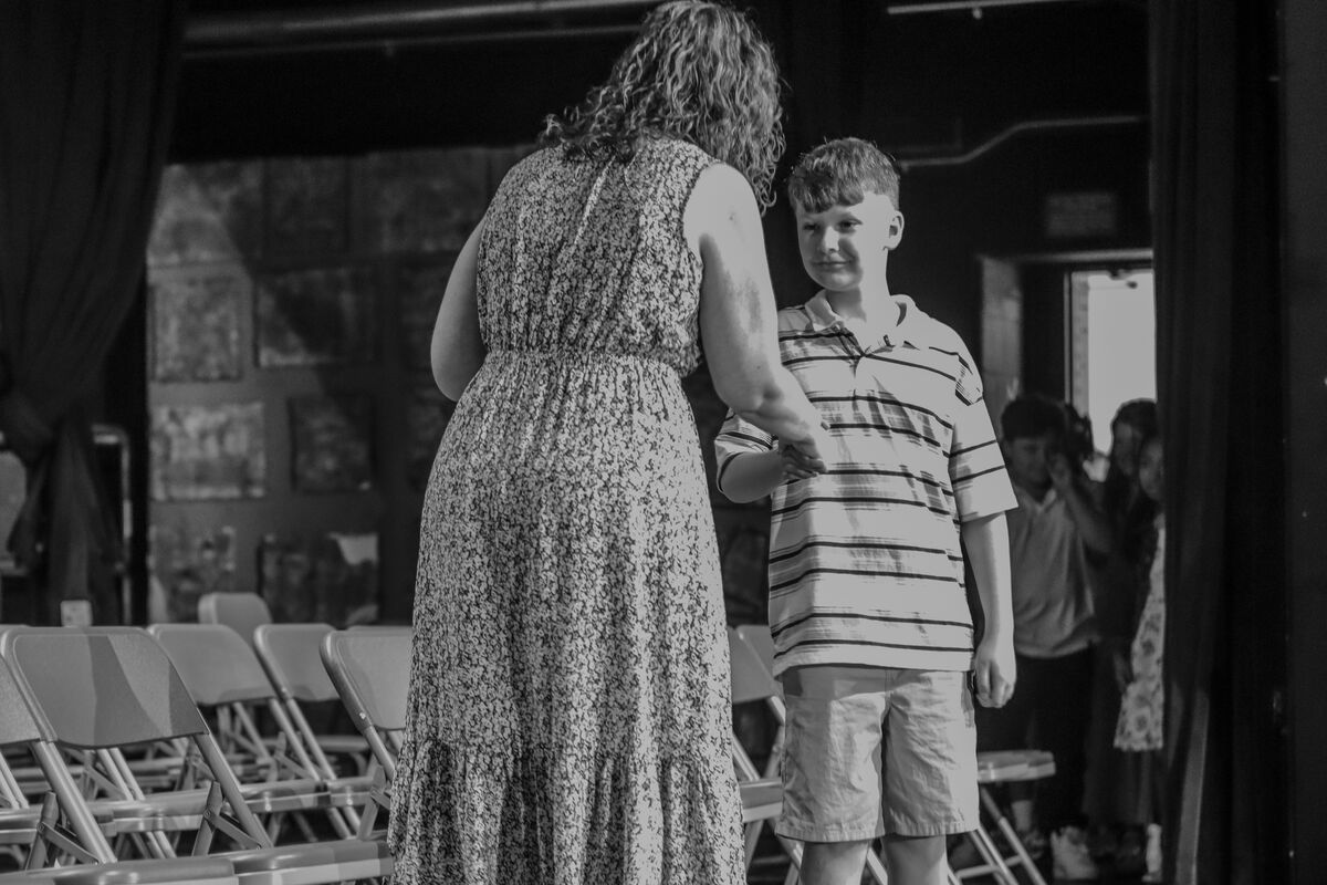 A woman in a floral dress shakes hands with a young boy in a striped shirt.