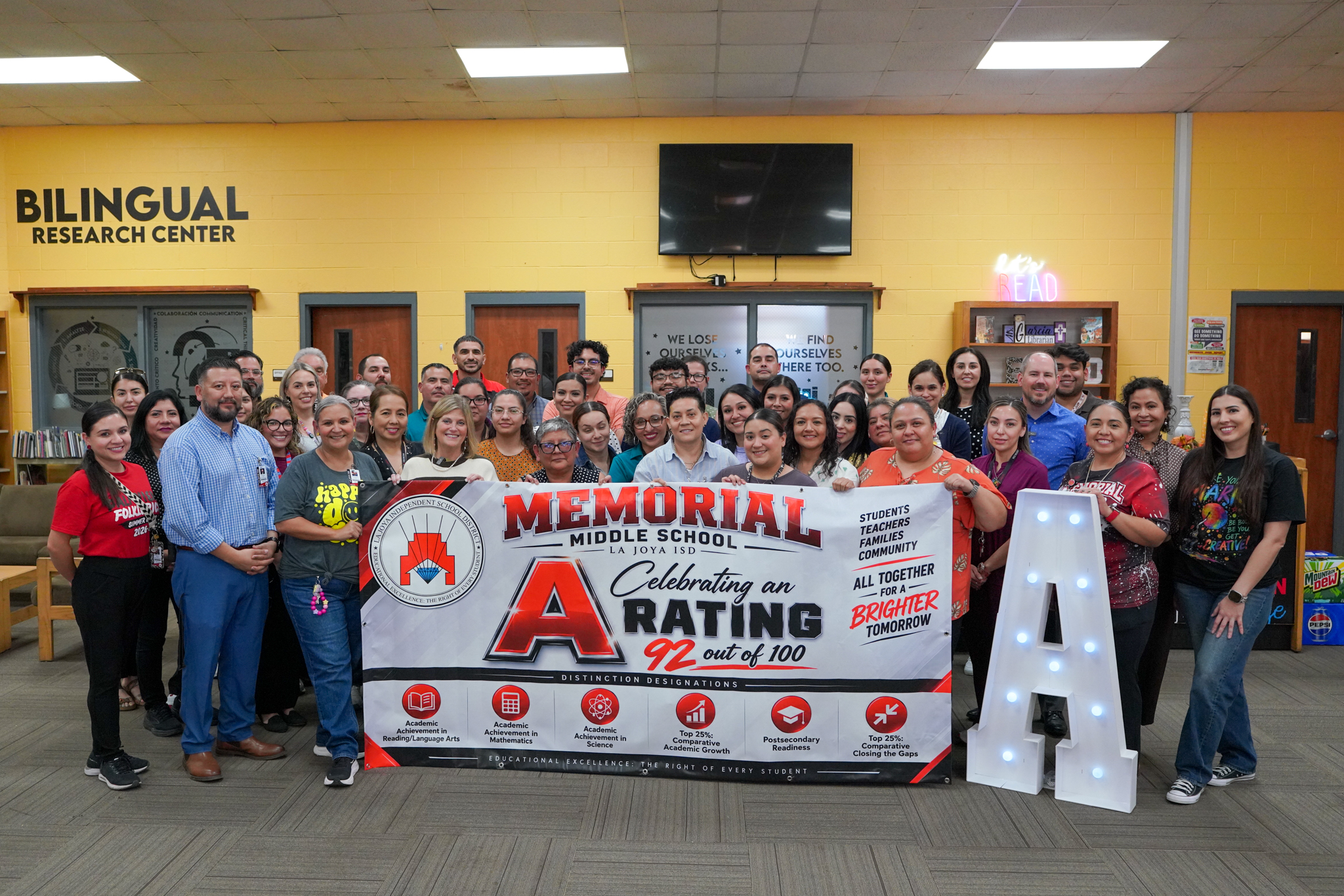 A diverse group of school staff and teachers proudly pose behind a banner celebrating Memorial Middle School's 'A' rating.