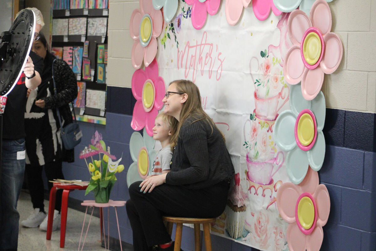 A woman and a child sit in front of a backdrop decorated with flowers and teacups for Mother's Day.