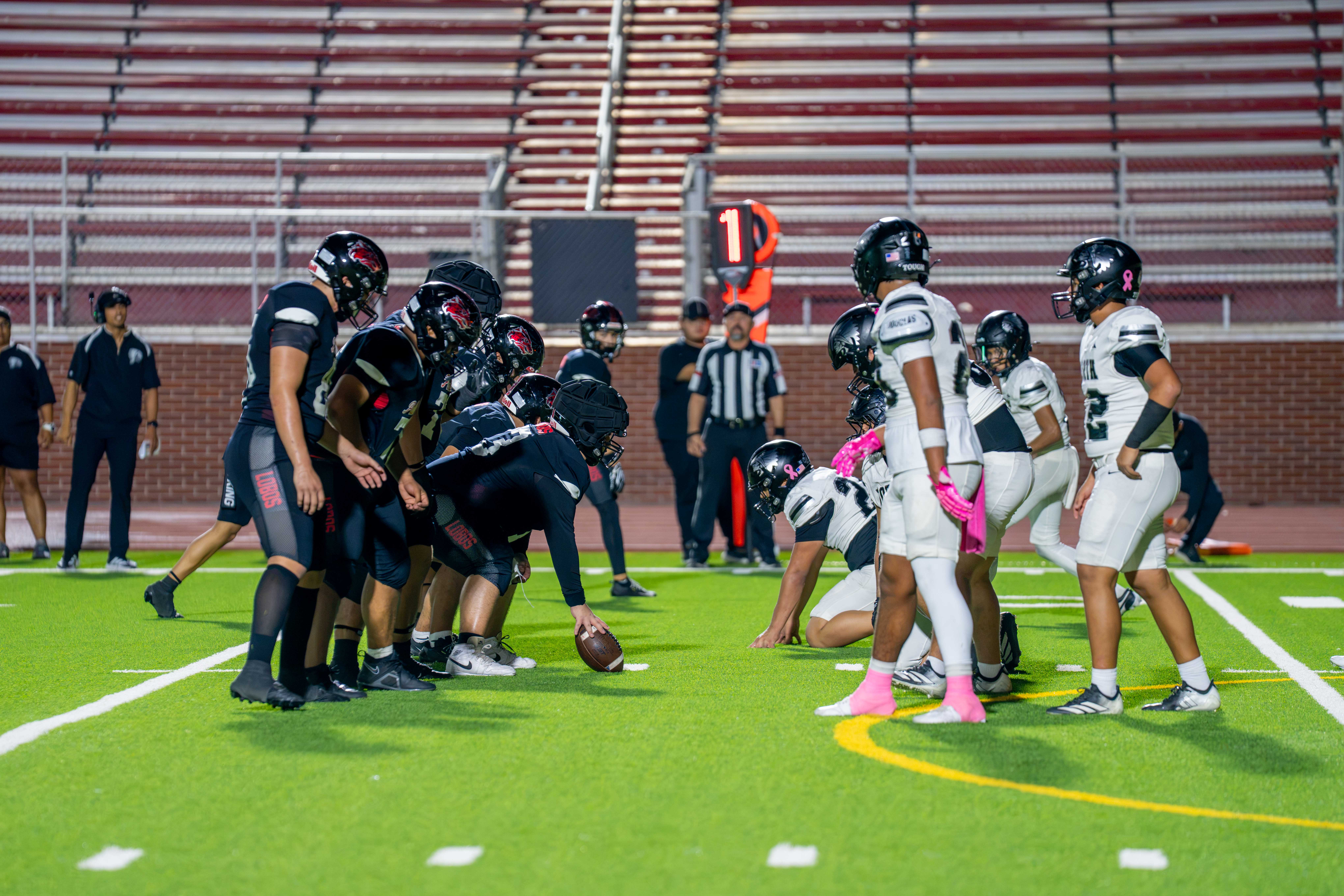 Two high school football teams line up face-to-face in a stadium for a night game.