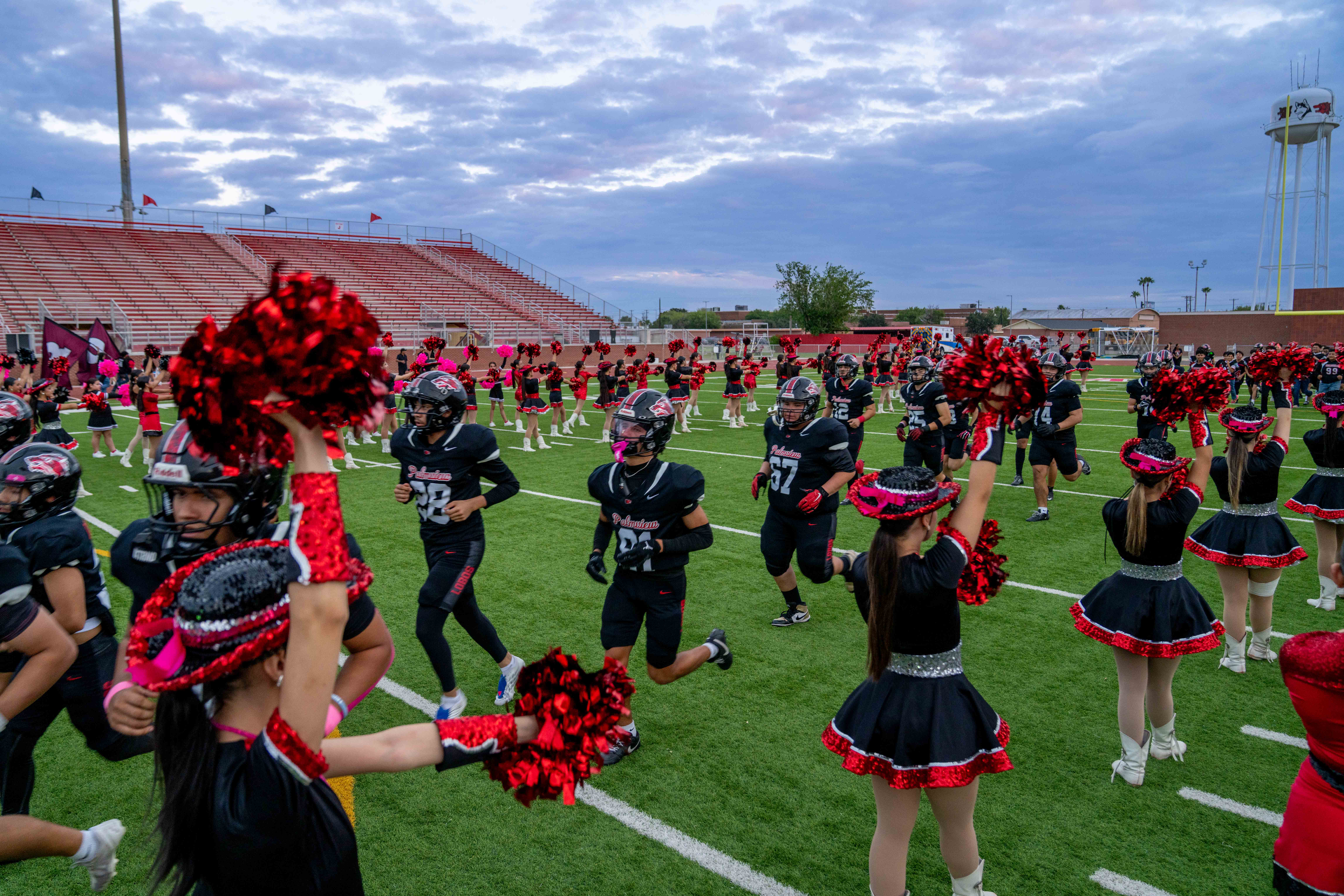 Football players in black uniforms run onto the field as cheerleaders in black and red outfits wave pom-poms.