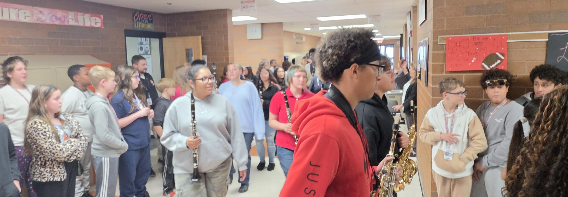 Students walk down a school hallway, some carrying instruments like clarinets and saxophones.