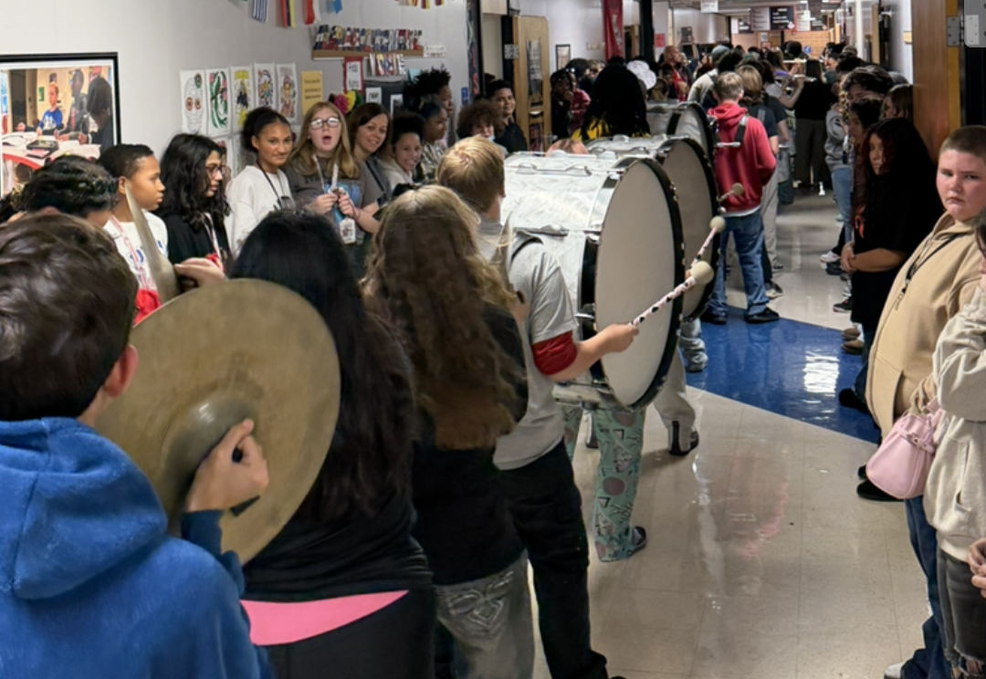 A school hallway is packed with students and marching band members carrying instruments.