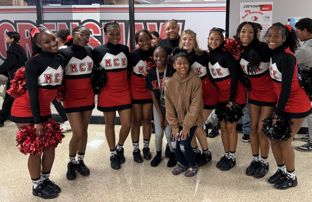 A group of diverse teenagers in red and black cheerleading uniforms pose together indoors.