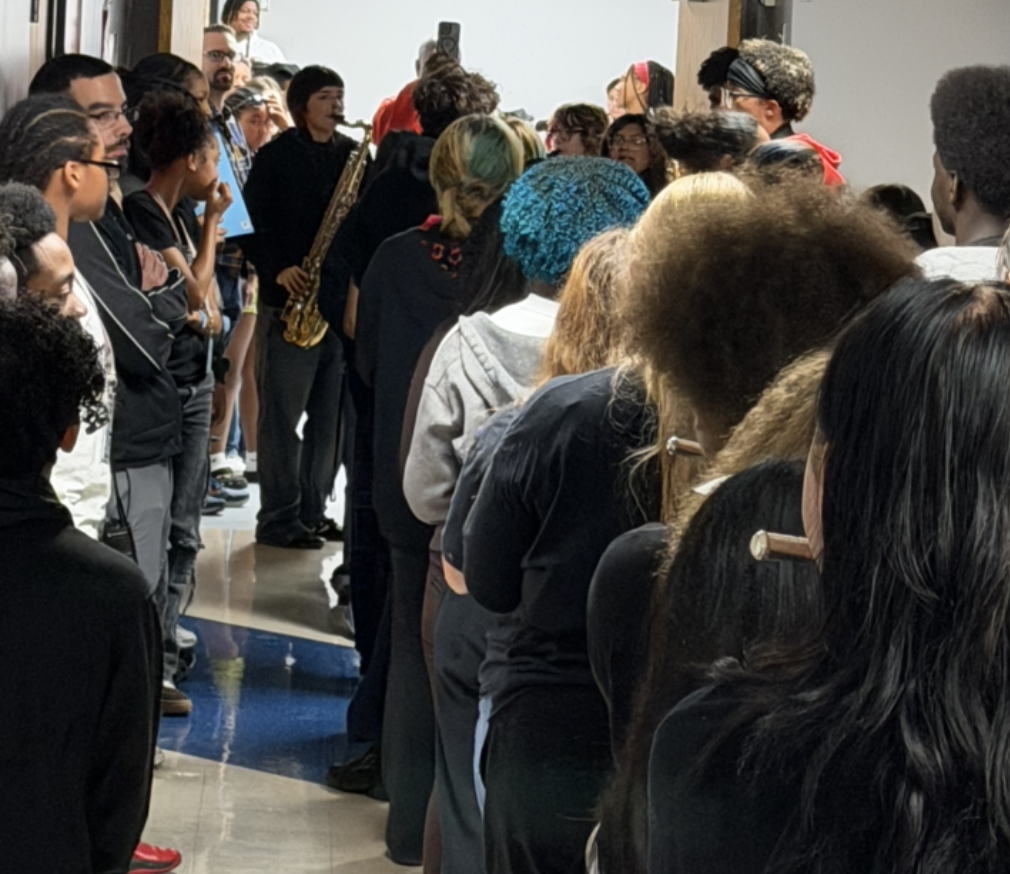 A crowded hallway filled with students and adults facing forward, some holding musical instruments.