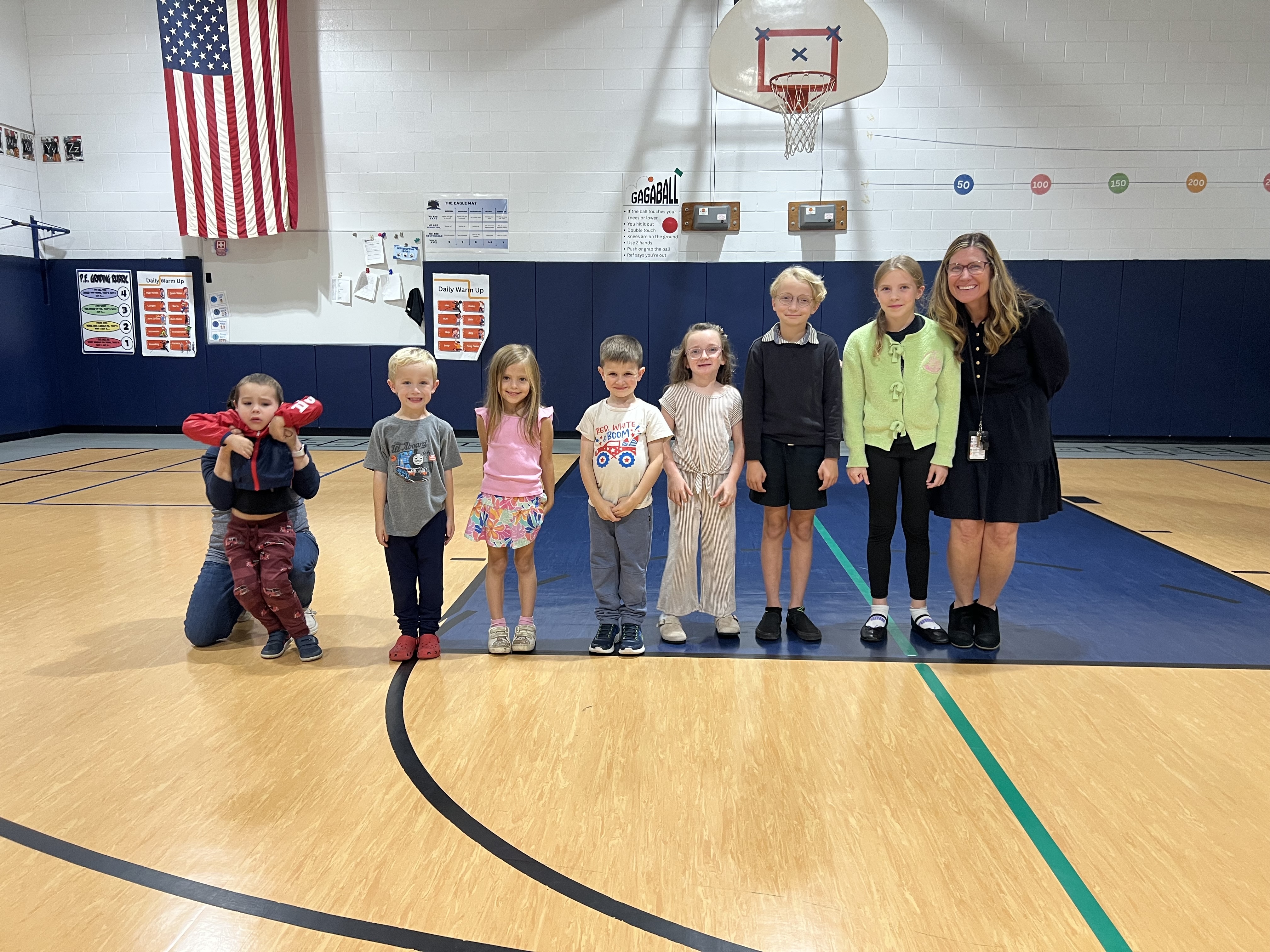 A teacher and students pose for a group photo inside a school gymnasium.
