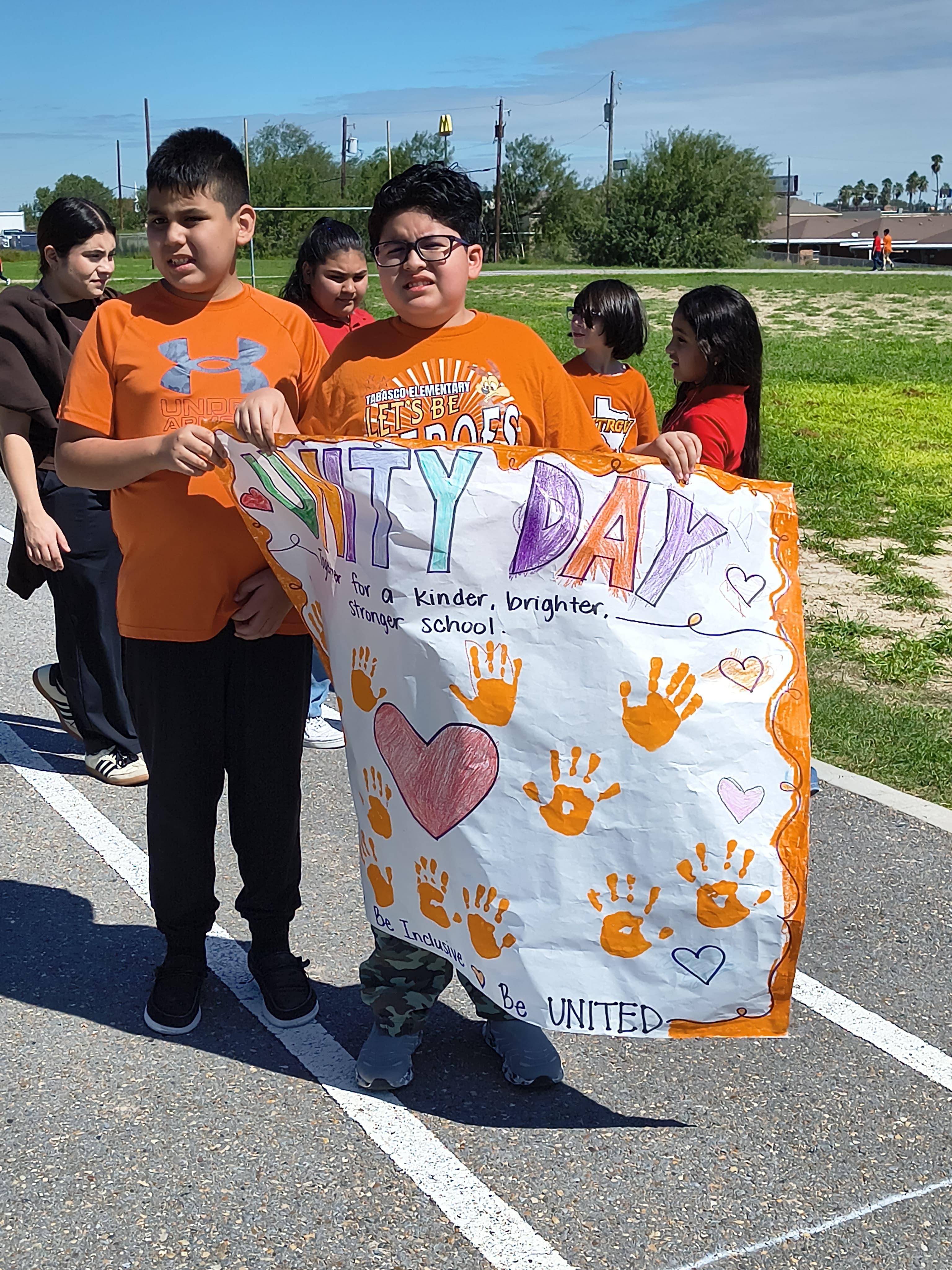 A group of students proudly hold a large banner that reads "UNITY DAY" on an outdoor track.
