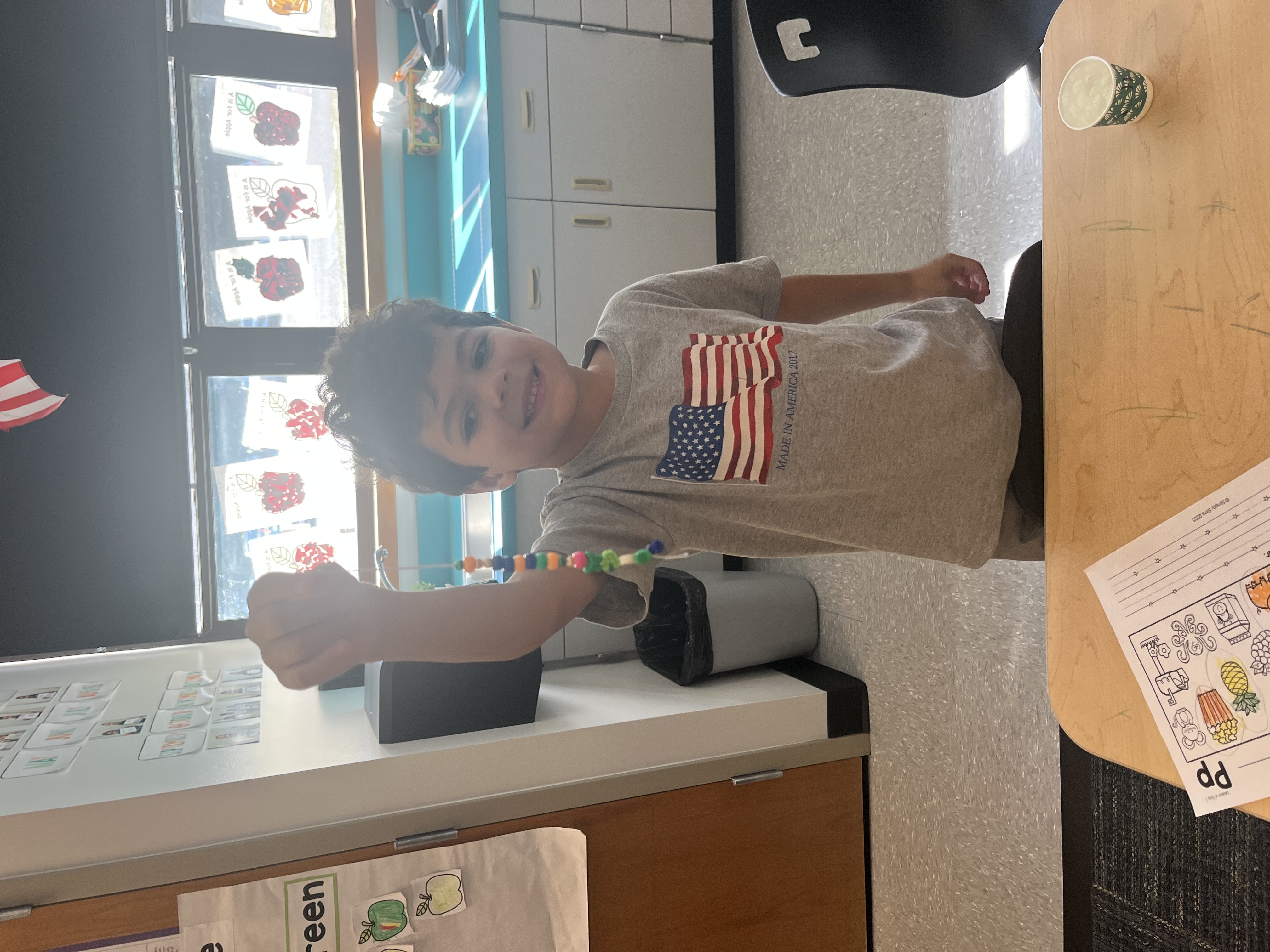 A smiling child holds up a string of colorful beads in a classroom.