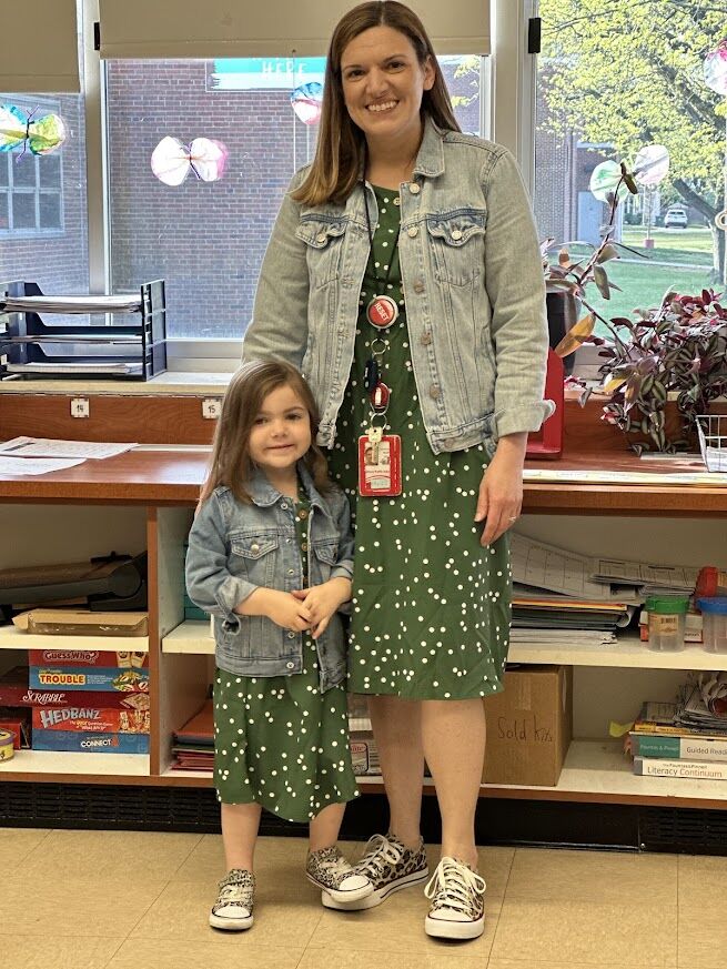 A woman and a young girl stand side-by-side, both wearing matching green polka dot dresses and denim jackets.