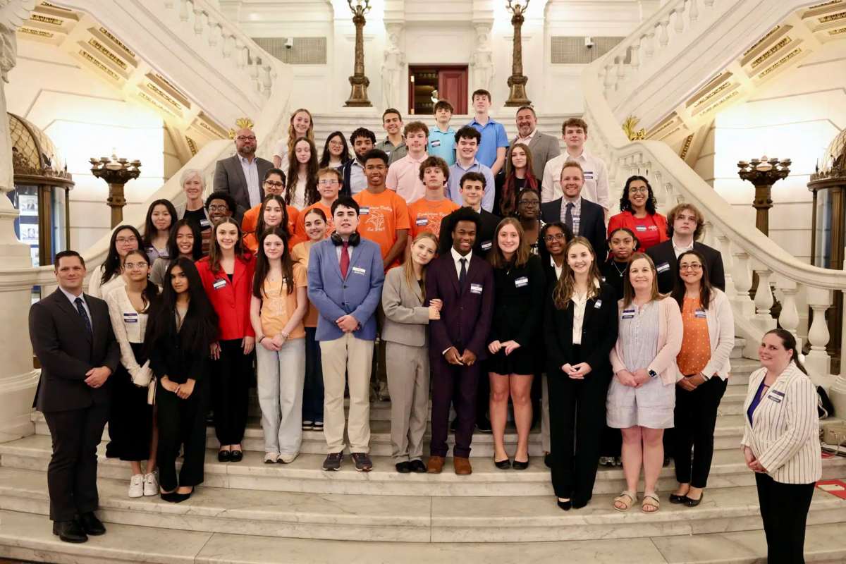 A diverse group of young people and adults pose for a photo on a grand staircase.