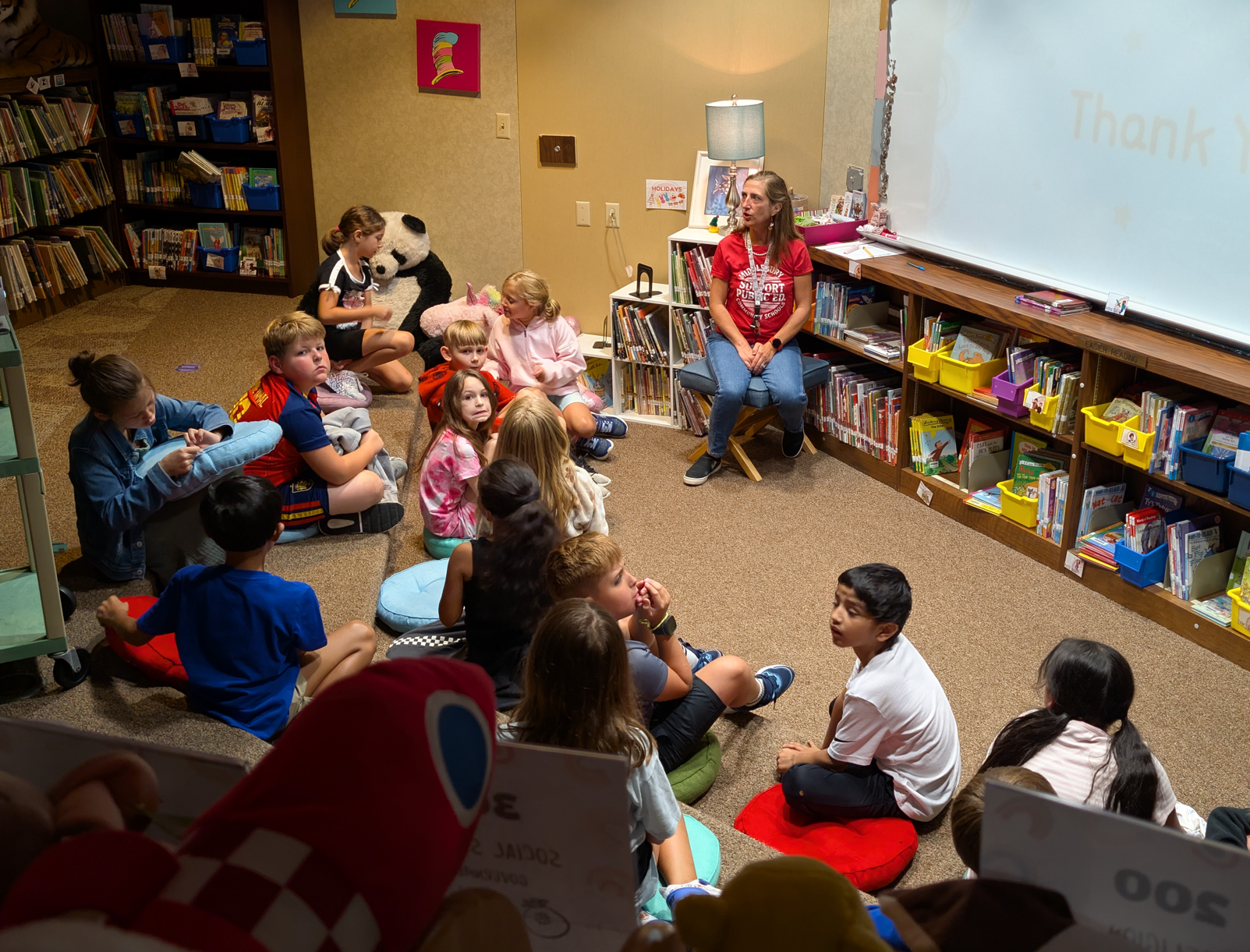 A teacher reads to a group of children sitting on the floor in a library.