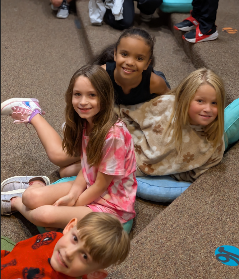 Four children sit together on floor cushions, smiling at the camera.