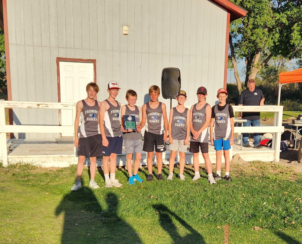 Seven young track athletes in Fremont Hawks uniforms pose together, holding a trophy outside.