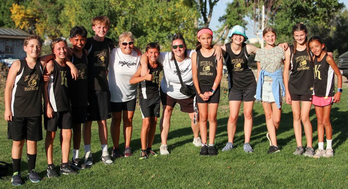 A group of young athletes and two coaches pose together outdoors, smiling in their black and gold track uniforms.