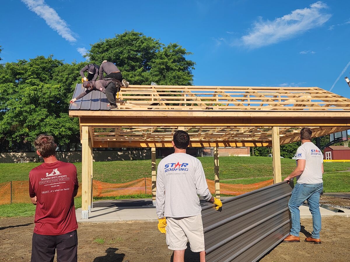 A team of construction workers installs a metal roof on a wooden pavilion on a sunny day.