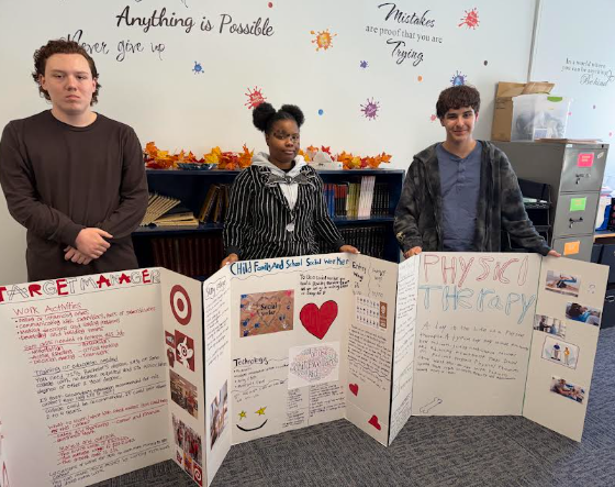 Three students stand behind their career research presentation boards in a classroom.