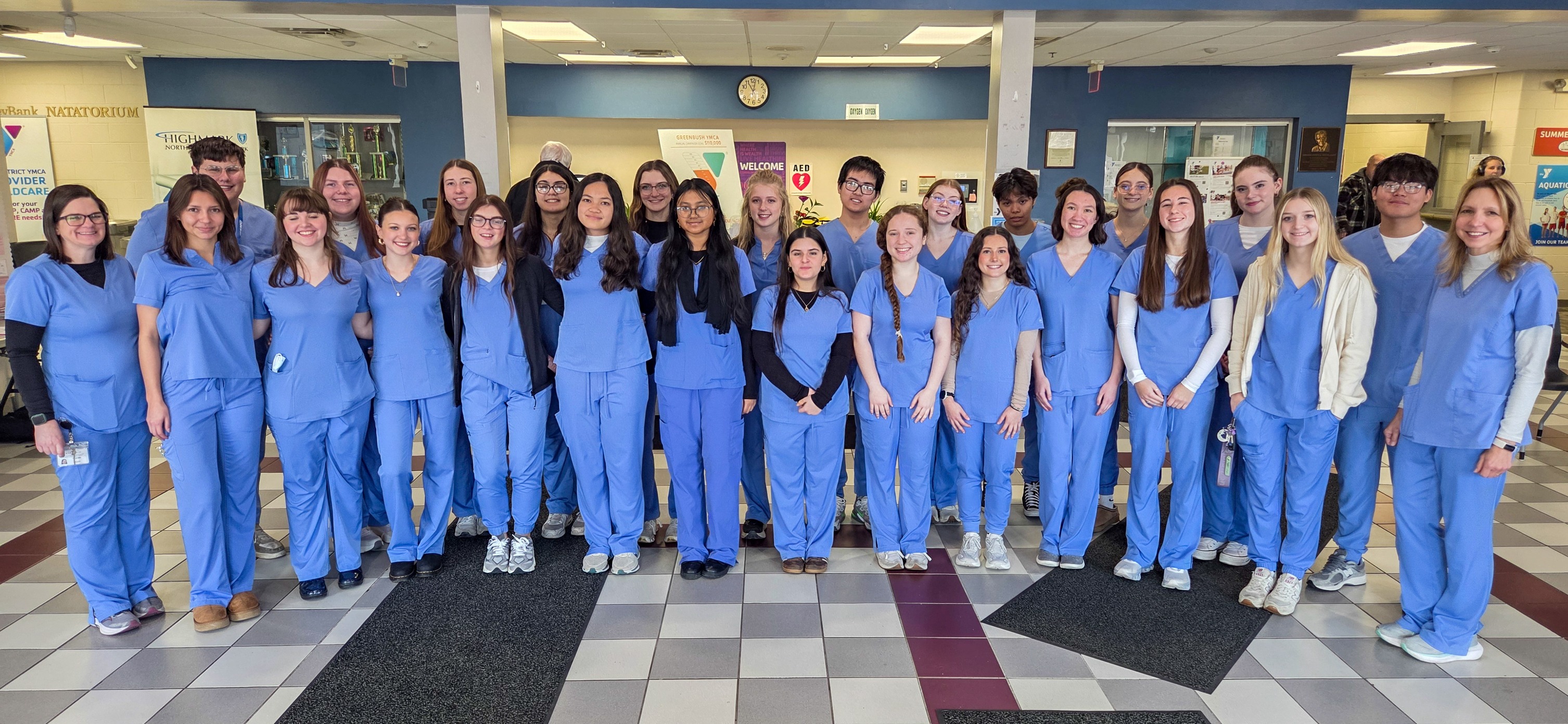 A diverse group of young adults in light blue scrubs stand together, posing for a photo.