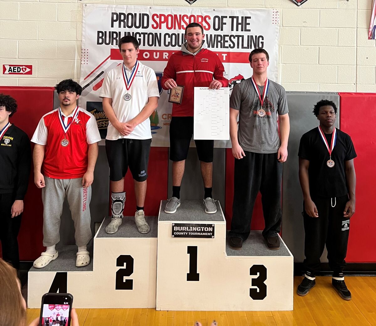Wrestlers stand on a podium, receiving medals and awards at the Burlington County Tournament.