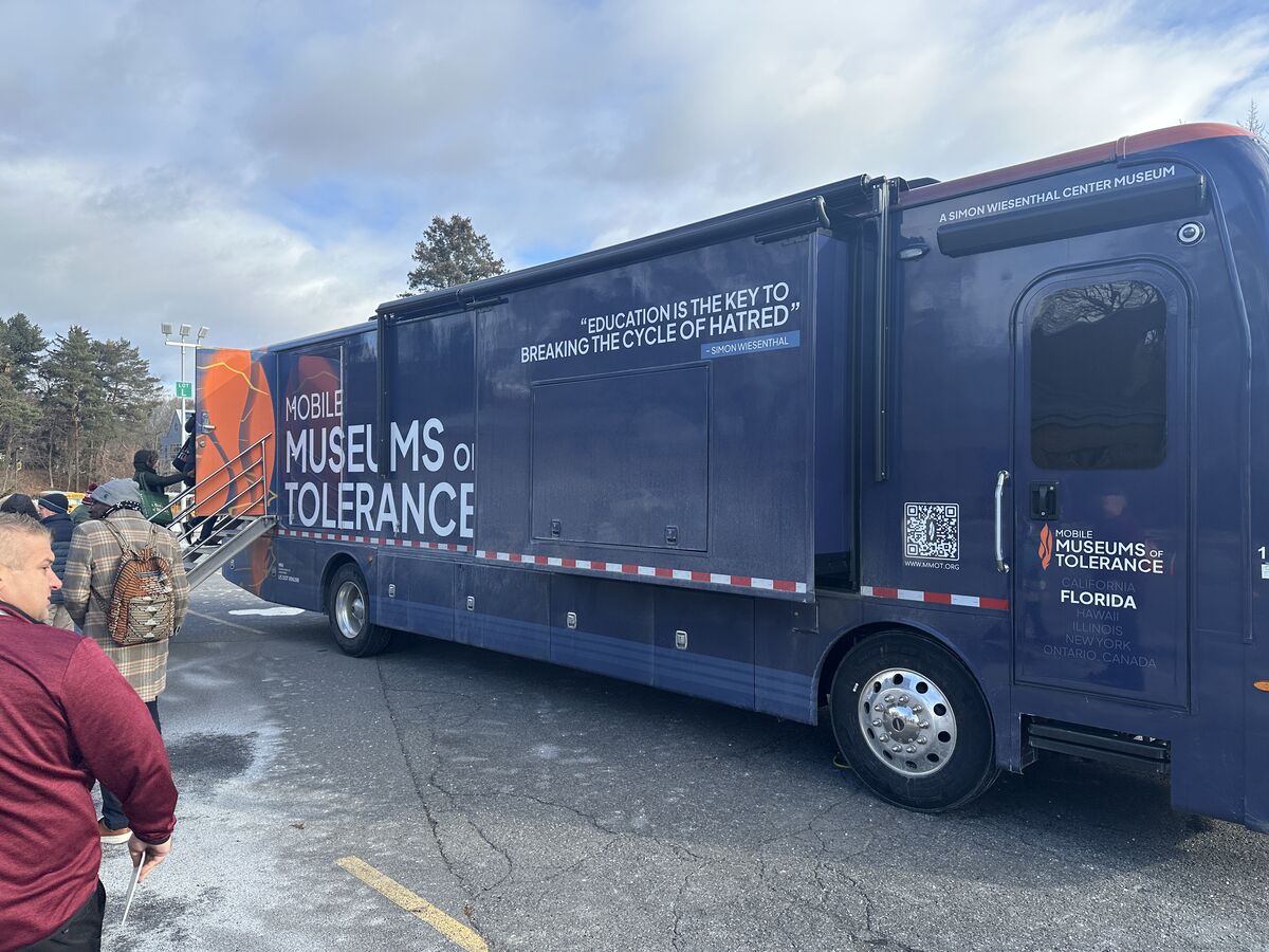 A dark blue mobile museum, the "Museums of Tolerance," is parked outdoors with people boarding via a ramp.
