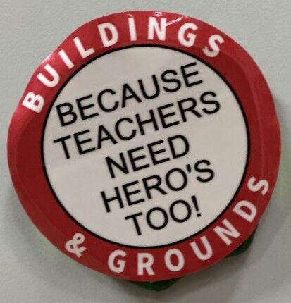 A round button with text that reads 'BUILDINGS & GROUNDS BECAUSE TEACHERS NEED HERO'S TOO!'.