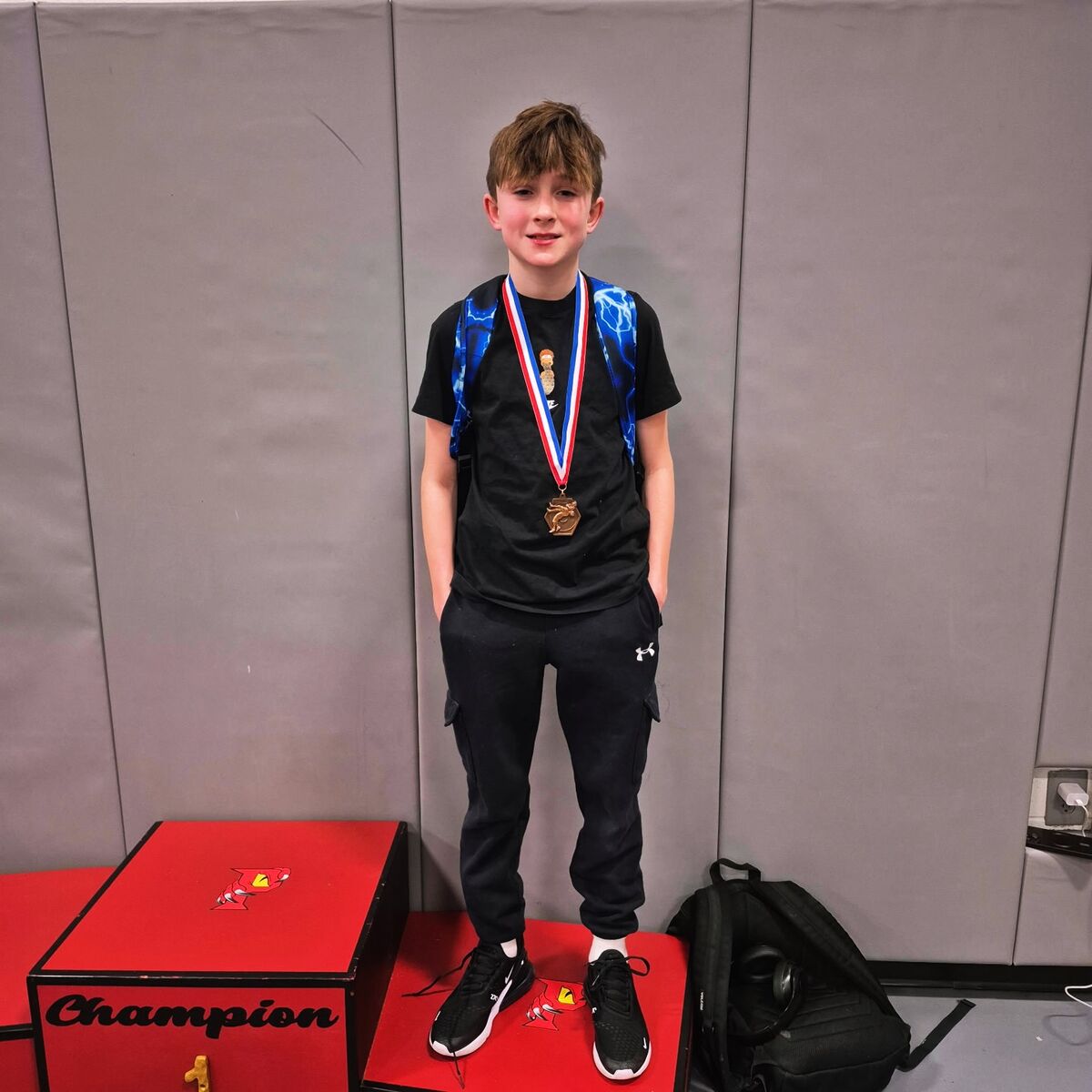 A young boy stands proudly on a red podium, wearing a medal around his neck.