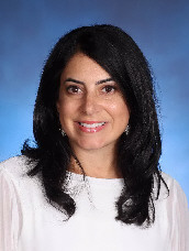 A woman with dark hair and a white top smiles at the camera.