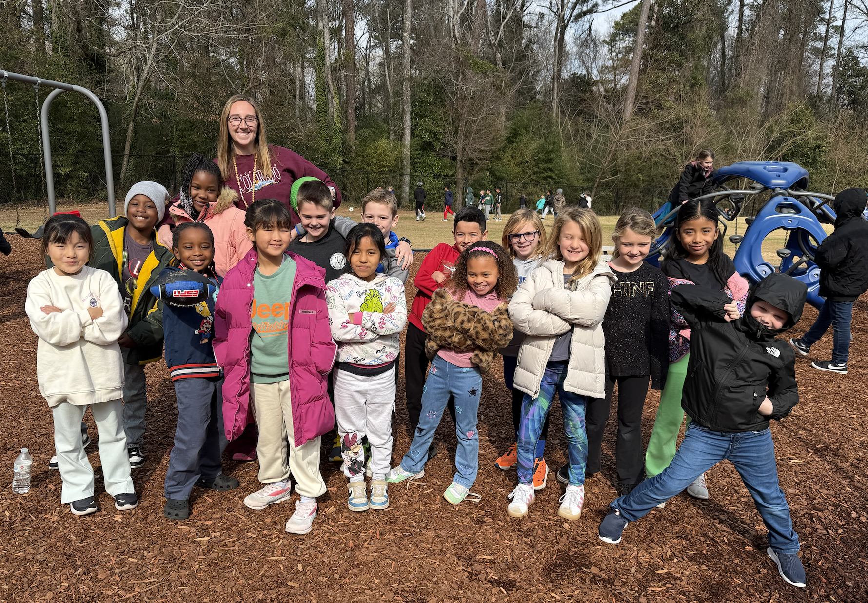 A diverse group of elementary school children and their teacher pose for a photo on a playground.