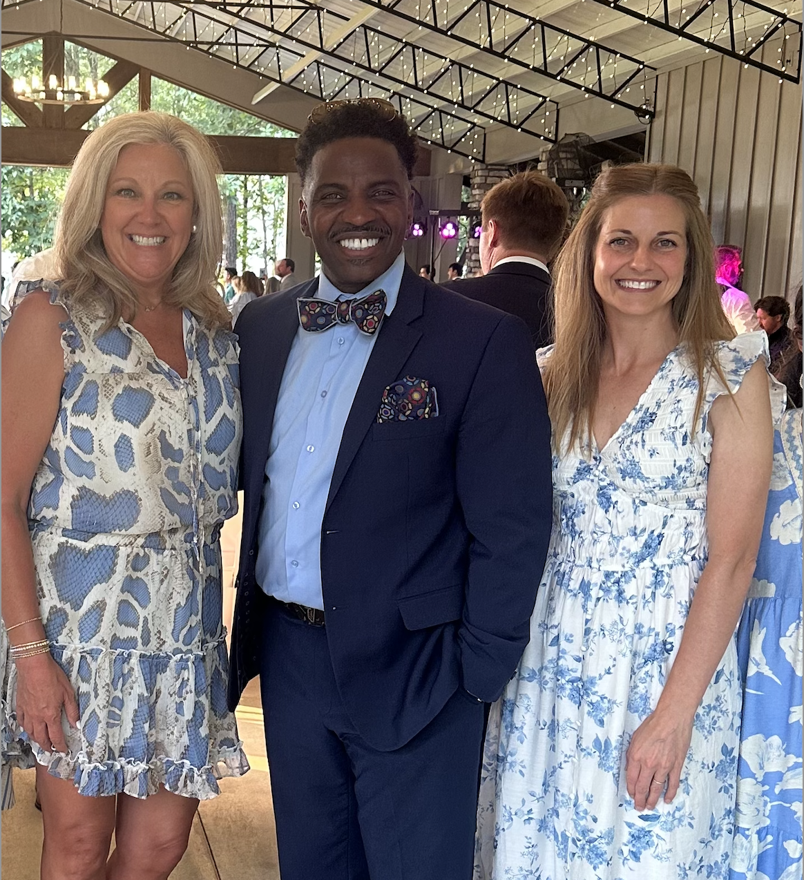 Three smiling people pose for a photo at an indoor event with decorative lighting.