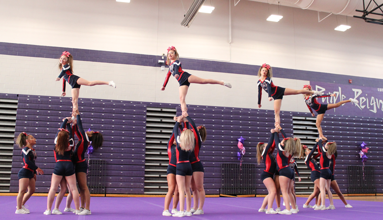 A cheerleading team performs a pyramid stunt with several members in the air.