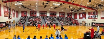 A panoramic view of a high school gymnasium during a basketball game with spectators in the stands.