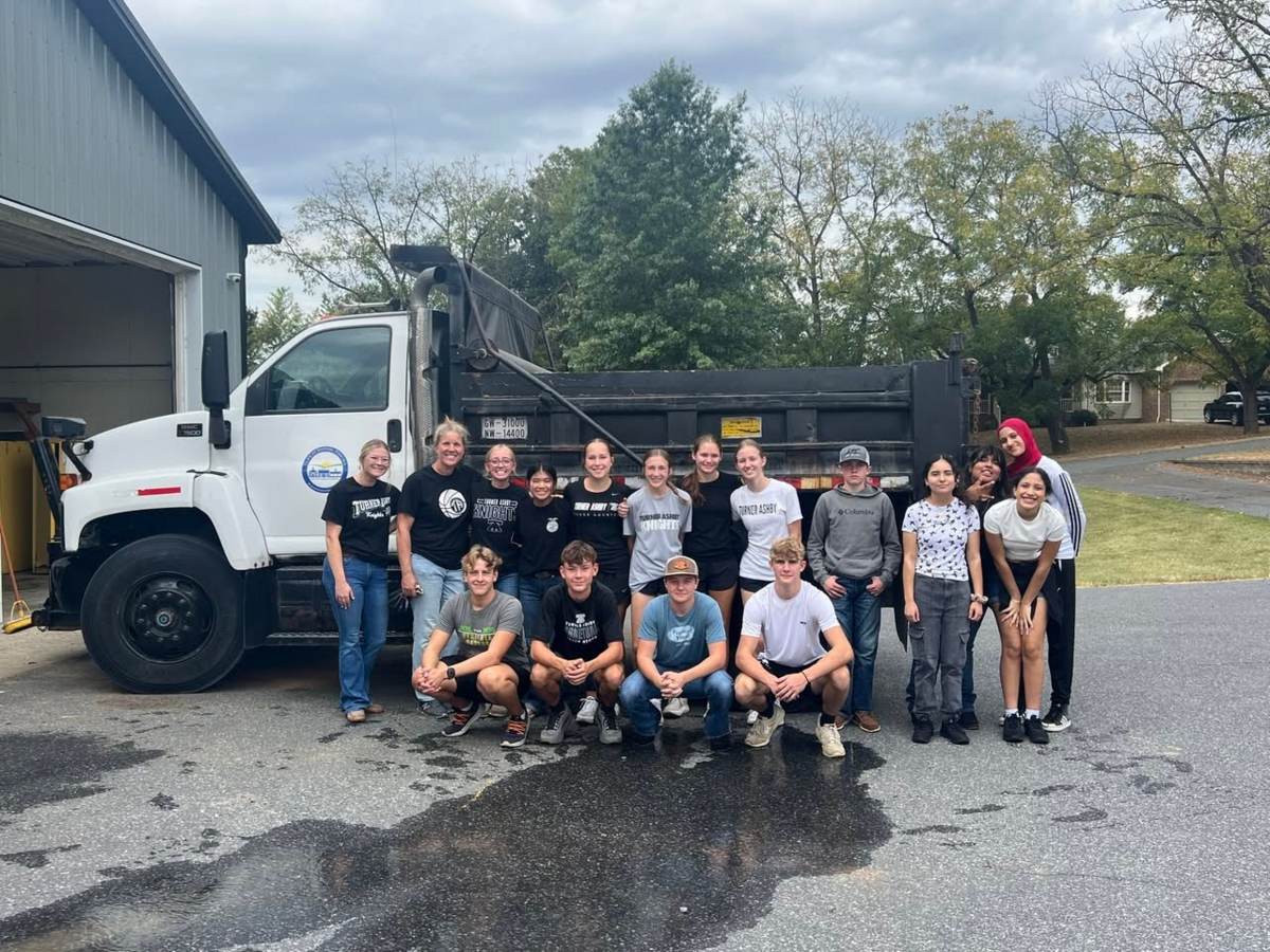 A group of students and adults stand in front of a large white dump truck.