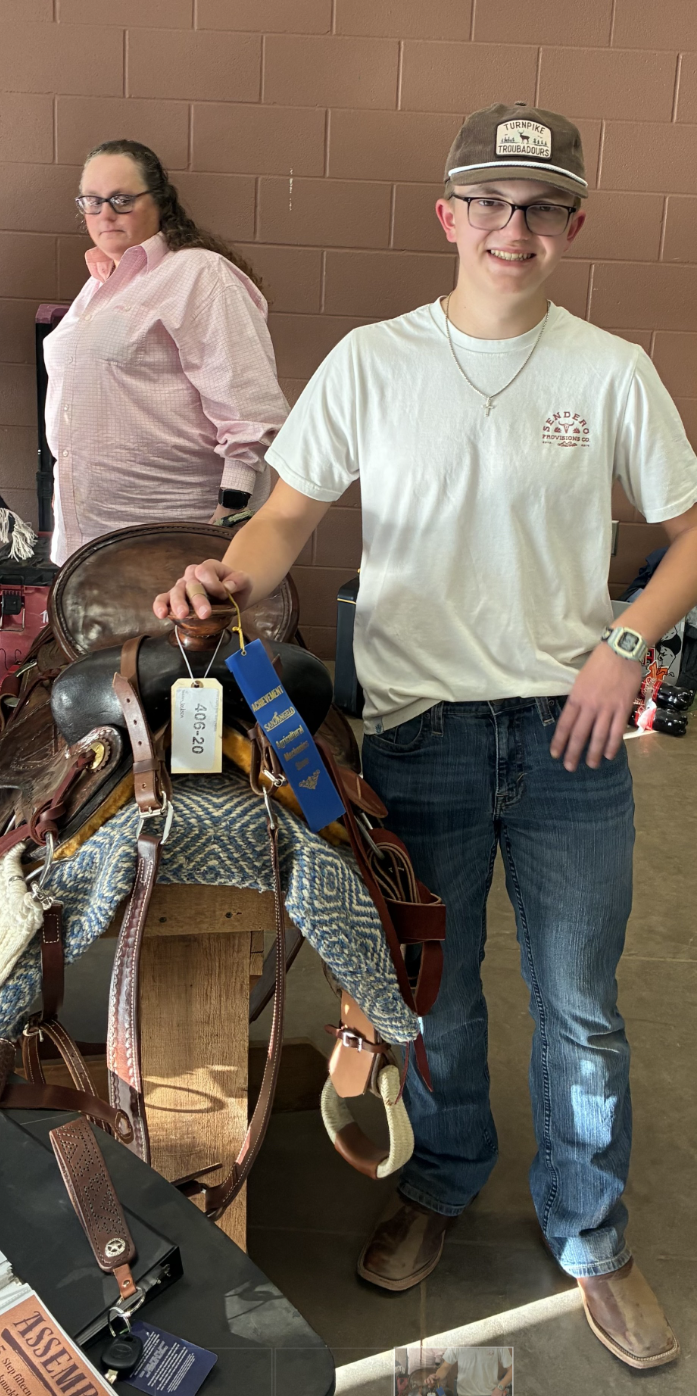 A young man in a cap and t-shirt proudly displays a saddle with blue and yellow ribbons.