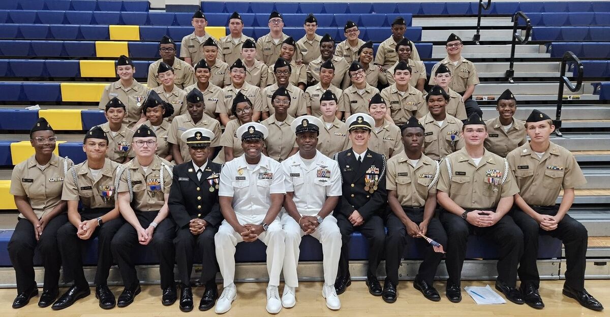 A diverse group of young people in navy-style uniforms pose for a photo on bleachers.