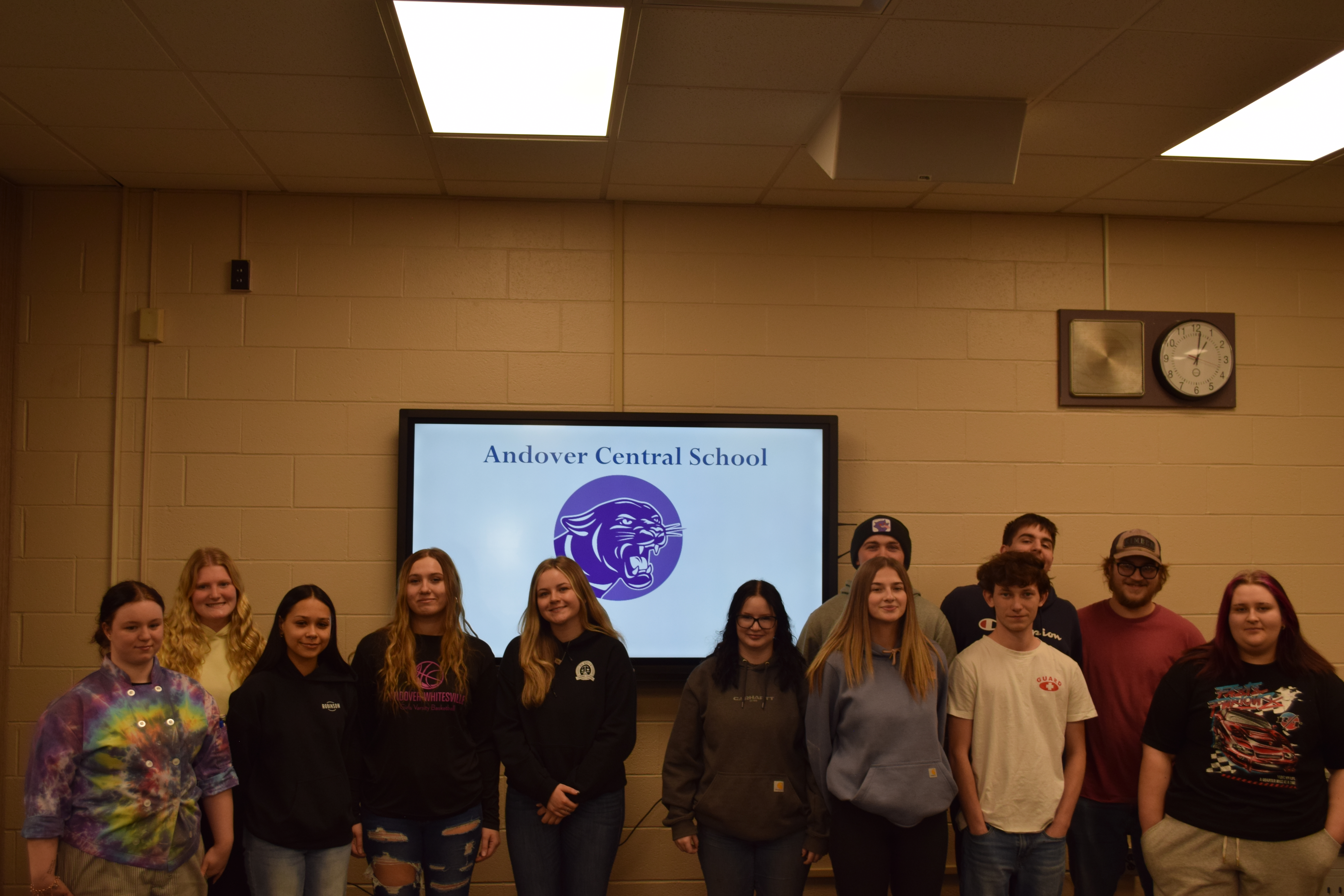 A group of students stand in front of a screen displaying "Andover Central School" and a panther logo.