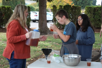 A volunteer serves a student a helping of the freshly pressed cider.
