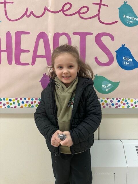 A young child smiles in front of a "Sweet Hearts" banner with bird decorations.