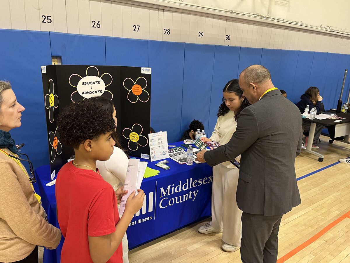 A man in a suit discusses information with a young woman at a table with a blue tablecloth that says 'Middlesex County'.