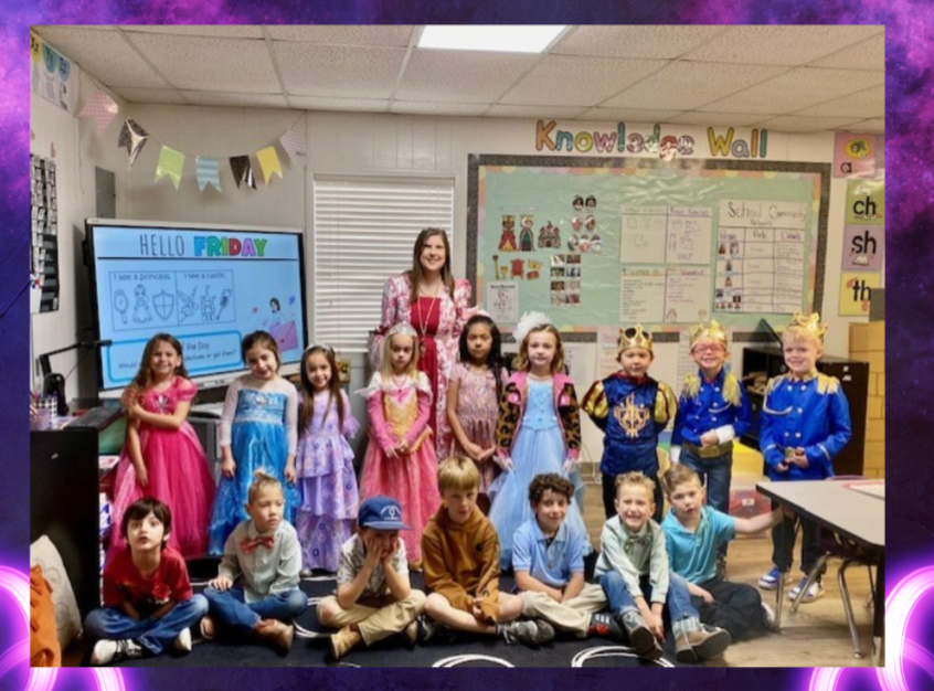 A teacher and students dressed as princesses and princes pose for a photo in a classroom.