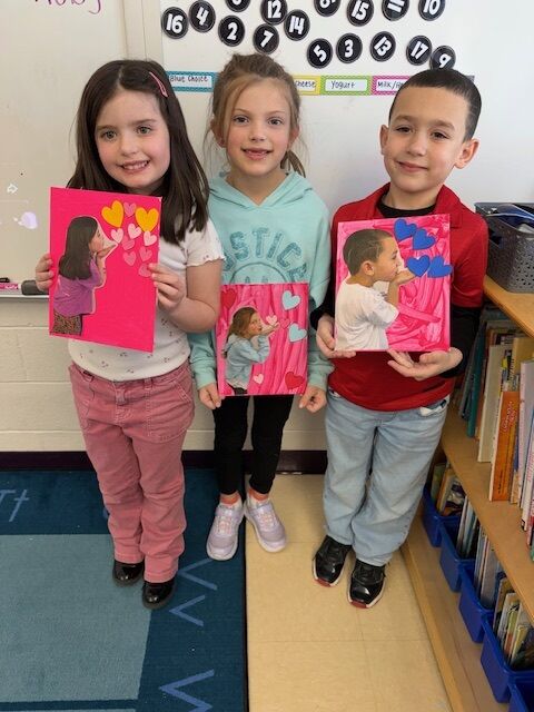 Three children proudly display their artwork featuring blowing kisses and hearts.