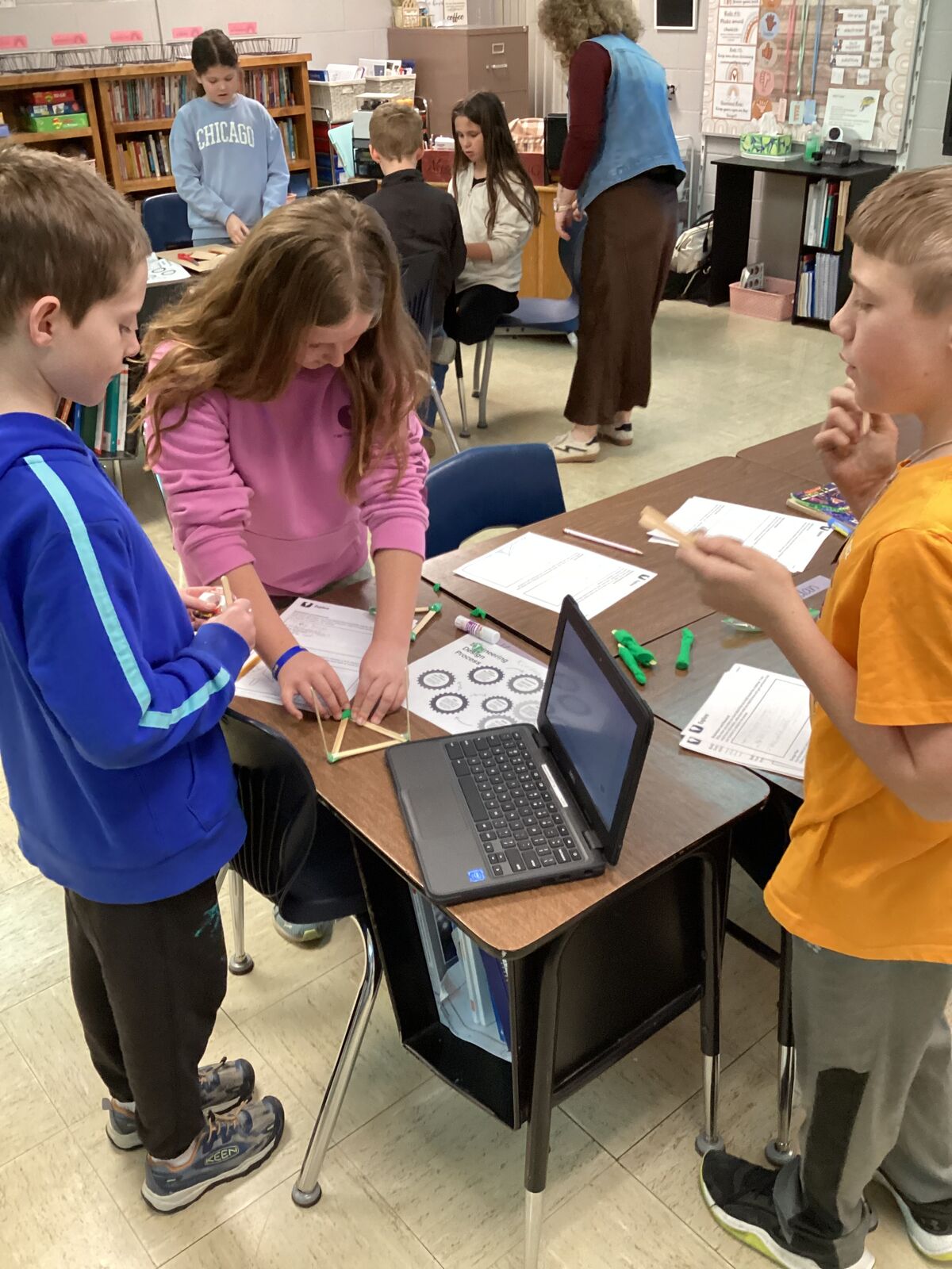 Students work together on a STEM project at desks with laptops and building materials.